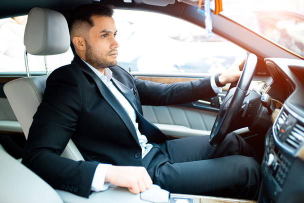 portrait of handsome young man sitting in bright salon of executive car - Fotoğraf, Görsel