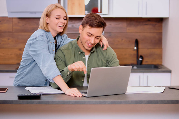happy couple at home use laptop, young husband discussing contract details with smiling wife - Foto, Imagen