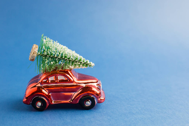 Κόκκινο αυτοκίνητο παιχνίδι με ένα χριστουγεννιάτικο δέντρο στην οροφή, μπλε φόντο τάση. Χρώμα του έτους - Φωτογραφία, εικόνα