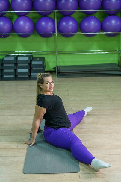 A fat woman is engaged in fitness in the gym. A girl with a lot of overweight trying to lose weight with the help of sports, does stretching exercises. - Photo, Image