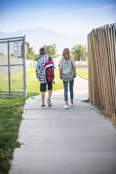 Vista de trás de um dois alunos do ensino fundamental caminhando para a escola juntos - Foto, Imagem