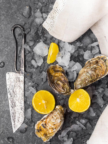 fresh raw oysters on ice with lemon slices, mollusk of the Atlantic Ocean on linen towel, knife - Foto, afbeelding
