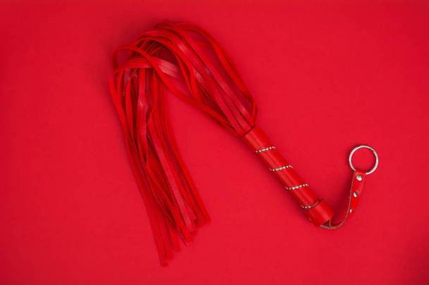 Látigo rojo sobre fondo de seda roja. Accesorios para juegos sexuales para adultos. Juguetes para BDSM
 - Foto, Imagen
