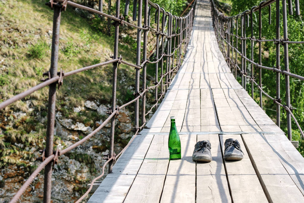 στη γέφυρα ανάρτησης κατά μήκος του ποταμού υπάρχουν παπούτσια και ένα πράσινο μπουκάλι - Φωτογραφία, εικόνα