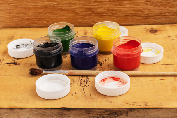 Open jars of gouache paint on a wooden background. Nearby lies a brush. - Foto, immagini