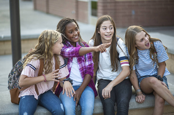 Photo amusante d'un groupe d'adolescentes qui socialisent, rient et parlent ensemble à l "école. Un groupe multiethnique de vrais élèves du premier cycle du secondaire - Photo, image
