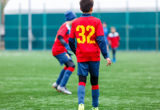 Kırmızı ve mavi spor giyimli çocuklar sahada futbol oynuyor, top sürüyor. Yeşil çimlerde top oynayan genç futbolcular. Eğitim, futbol, çocuk konsepti için aktif yaşam tarzı - Fotoğraf, Görsel