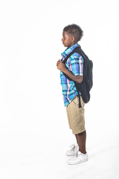 Afroamerykanin na białym tle. Ubrany w plecak i koszulę w kratę i gotowy do szkoły. widok z boku - Zdjęcie, obraz