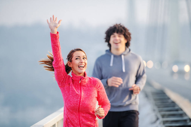 橋の上を走るスポーツウェアで幸せな白人夫婦を笑顔。冬だアウトドアフィットネスのコンセプト. - 写真・画像