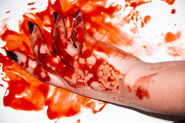 A Female hand in the blood. A Black manicure and the blood around.Terrible and bloody background. - Photo, Image