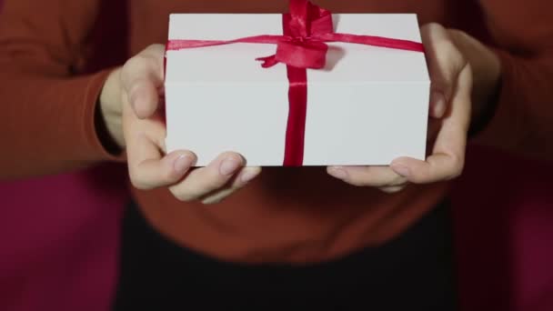 Beautiful girl holds out a gift in a white box ,with a red ribbon. Beautiful girl hands hold a New Years gift, in a white box with a red ribbon. Gift for the holiday. - Séquence, vidéo
