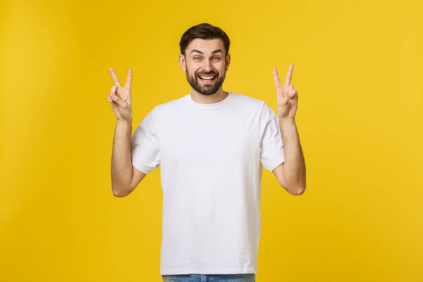 Joven hombre guapo con camiseta a rayas sobre fondo amarillo aislado sonriendo mirando a la cámara mostrando los dedos haciendo señal de victoria. Número dos.
 - Foto, Imagen