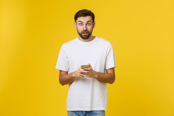 Хорошие новости от друга. Уверенный молодой красивый мужчина в джинсовой рубашке держит смартфон на желтом фоне
 - Фото, изображение