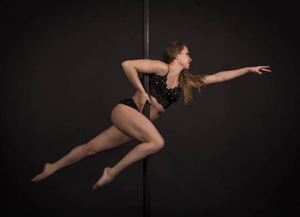 Athletic girl with long hair performs exercises on a portable pole in a black swimsuit. - Fotó, kép