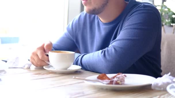 Morning coffee. Cropped caucasian man in blue drinking coffee ot tea in restaurant, cafe. Closeup man hands with white cup.  - Felvétel, videó