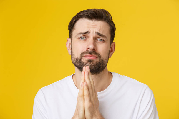 Young guy dressed casually isolated on yellow background, having put hands together in prayer or meditation, looking relaxed and calm. - Photo, Image