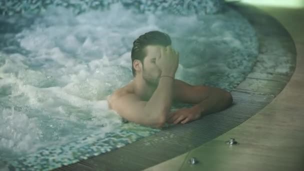 Homem sexy relaxando na piscina no hotel spa. Homem tocando cabelo molhado em jacuzzi no spa - Filmagem, Vídeo