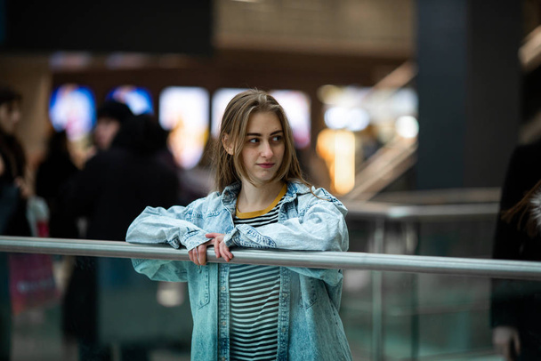 Teenager. Young pretty white caucasian teenage girl with long hair with problem skin and long hair in a shopping center near the railing. - Photo, image