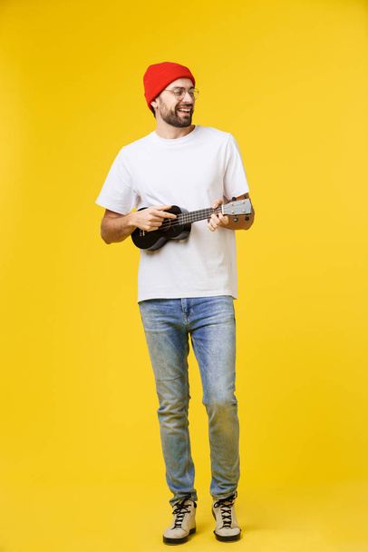 Guitarrista hombre toca en la guitarra eléctrica con emociones brillantes, aislado sobre fondo amarillo
. - Foto, Imagen