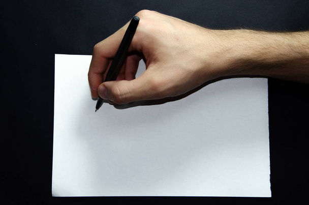Miehen vasen ja oikea käsi pitävät kynää valkoisen paperiarkin päällä mustalla pohjalla. Erät arkkia kohti, Urheilu ja Fitnec
 - Valokuva, kuva