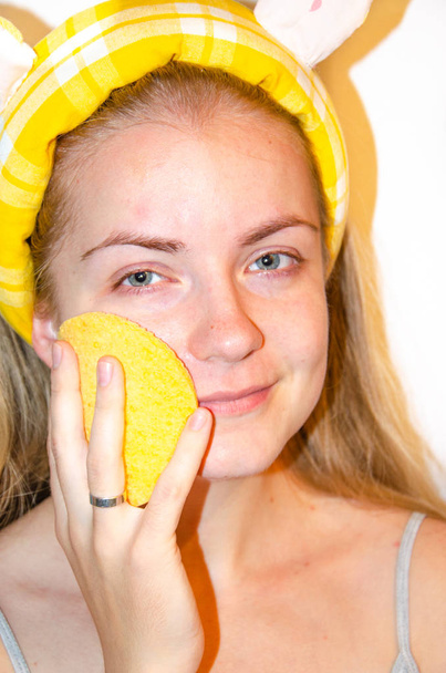 Evropská dívka si nanáší korejskou kosmetiku na obličejovou masku. Čistí póry, mastnotu, akné, vrásky. Detailní záběr na dívku s problémy s kůží. Mousse, sprej, obličejový drhnutí a omývání obličejů.Žlutá houba - Fotografie, Obrázek