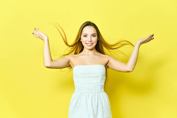 Portrait of charming young blonde woman, looking at camera with cute smile. Student girl relaxing indoors after college on yellow background. - Foto, imagen