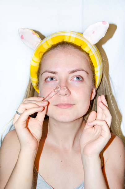 Een Europees meisje brengt Koreaanse cosmetica aan op haar gezichtsmasker. Reinigt poriën, vet, acne, rimpels. Close-up gezicht van een meisje met huidproblemen. Mousse, spray, gezichtsscrub en gezichtsspoeling.Gele spons - Foto, afbeelding