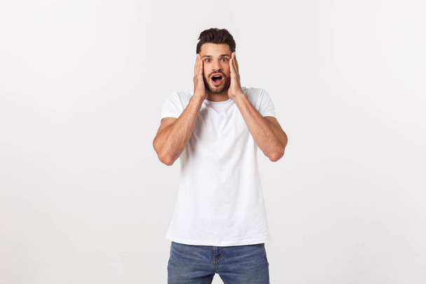 muž křičící ústa otevřená, držet hlavu ruku, nosit ležérní bílé tričko, izolované bílé pozadí, koncept tvář emoce - Fotografie, Obrázek