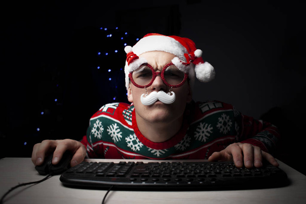 男は夜にコンピューターで遊ぶクリスマスの孤独な学生ゲーマーは、コンピュータの近くに座っている - 写真・画像