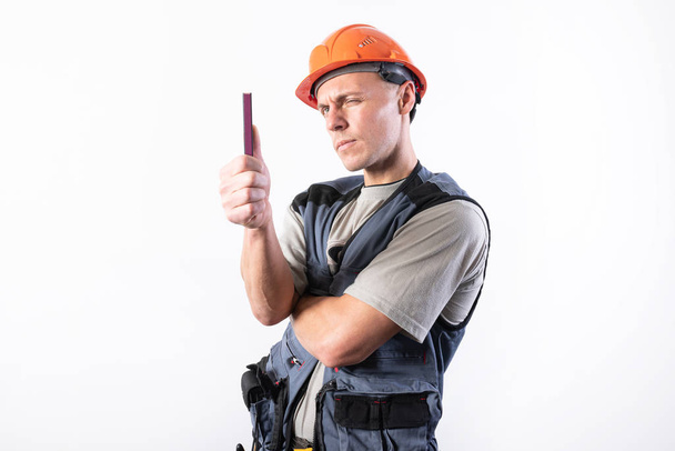 A builder in a helmet makes visual measurement with a marking pencil. - Photo, Image