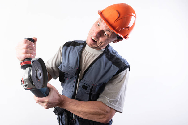 Builder with angle grinder, in a helmet, with a funny expression on his face. - Foto, imagen