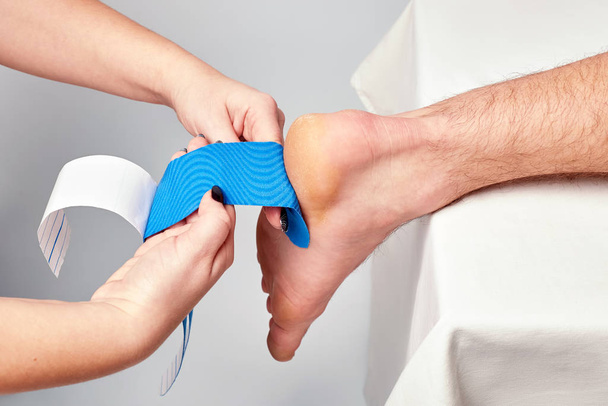 doctor physiotherapist hands applying kinesiology tape on the ankle of a caucasian man - 写真・画像
