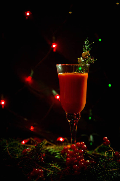 red Christmas glass with drink, cocktail decorated in new year style, green branch, clothespin and berry, on a dark background - Fotografie, Obrázek