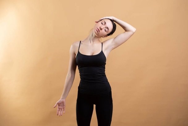 Retrato de vista lateral de una hermosa mujer joven con camiseta blanca haciendo ejercicio sobre fondo naranja, haciendo estiramiento
. - Foto, Imagen