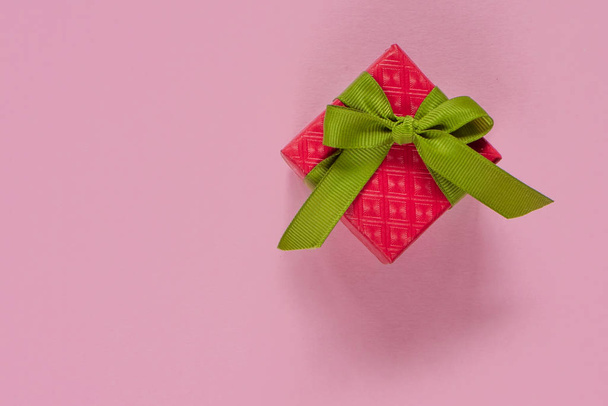 Red gift or present box with green ribbon on pink table top view. Flat lay. Birthday, wedding or christmas concept. - Valokuva, kuva
