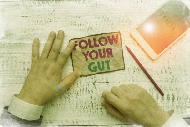 Text sign showing Follow Your Gut. Conceptual photo Listen to intuition feelings emotions conscious perception Hand hold note paper near writing equipment and modern smartphone device. - Fotoğraf, Görsel