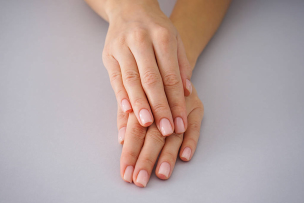 Female hands with a beautiful manicure on a gray background. - Valokuva, kuva