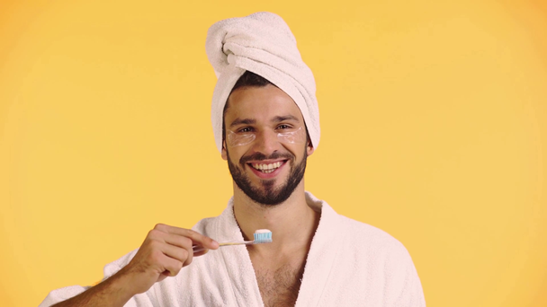 улыбающийся мужчина держит зубную щётку изолированной на жёлтом
 - Кадры, видео