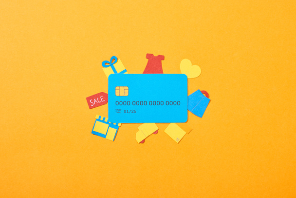 πάνω όψη του προτύπου μπλε πιστωτικής κάρτας κοντά σε εικονίδια αγορών που απομονώνονται σε πορτοκαλί - Φωτογραφία, εικόνα