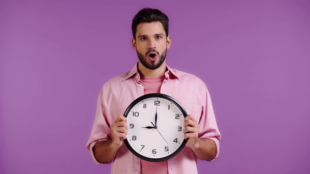 shocked man obscuring face with clock isolated on purple - Footage, Video
