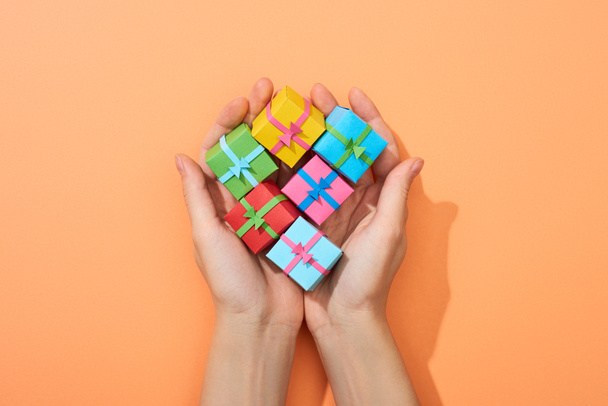 cropped view of woman holding multicolored small gift boxes on peach background - Фото, зображення