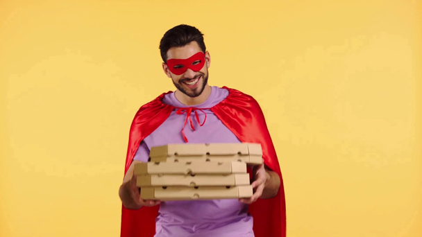 Gülümseyen süper kahraman, elinde pizza kutularıyla sarı kutular tutuyor. - Video, Çekim