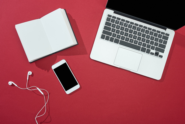 top view of smartphone, laptop, earphones, blank notebook on red background - Photo, Image