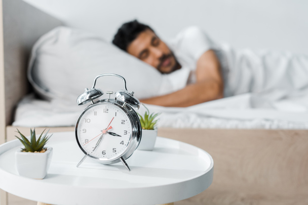 selective focus of alarm clock, plants and handsome bi-racial man sleeping on background  - Foto, imagen