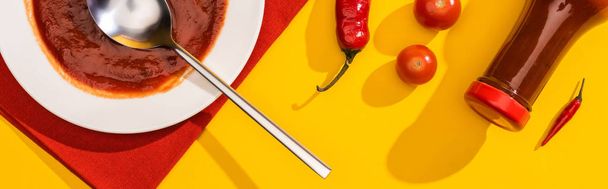 Bovenaanzicht van bord en fles met ketchup, chili pepers en kerstomaten op gele achtergrond, panoramisch shot - Foto, afbeelding
