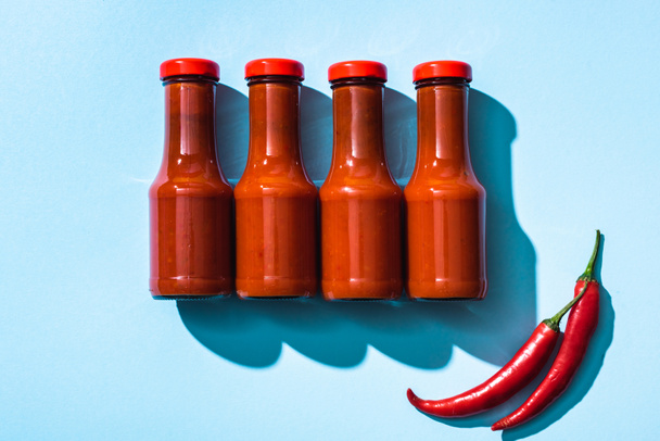 Horní pohled na chilli papričky a rajčatová omáčka v lahvích na modrém pozadí - Fotografie, Obrázek