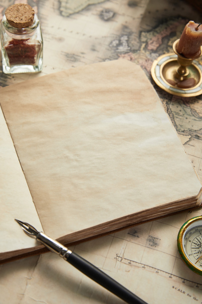 portátil en blanco vintage con pluma fuente cerca de brújula y vela en el fondo del mapa
 - Foto, Imagen