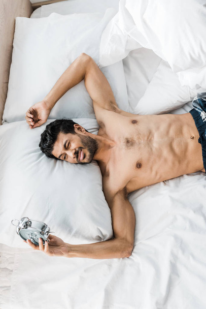 κορυφαία άποψη του σέξι και όμορφος bi-φυλετικός άνθρωπος κοιμάται στο κρεβάτι το πρωί  - Φωτογραφία, εικόνα