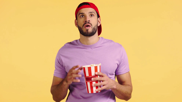 muž sleduje film a jíst popcorn izolované na žluté - Záběry, video