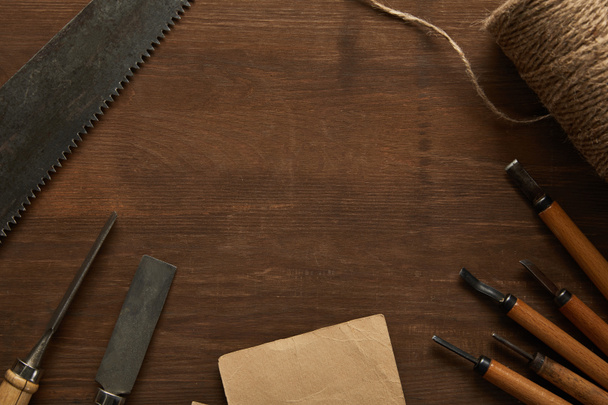 top view of aged carpentry tools and twine near blank vintage paper on wooden table - 写真・画像